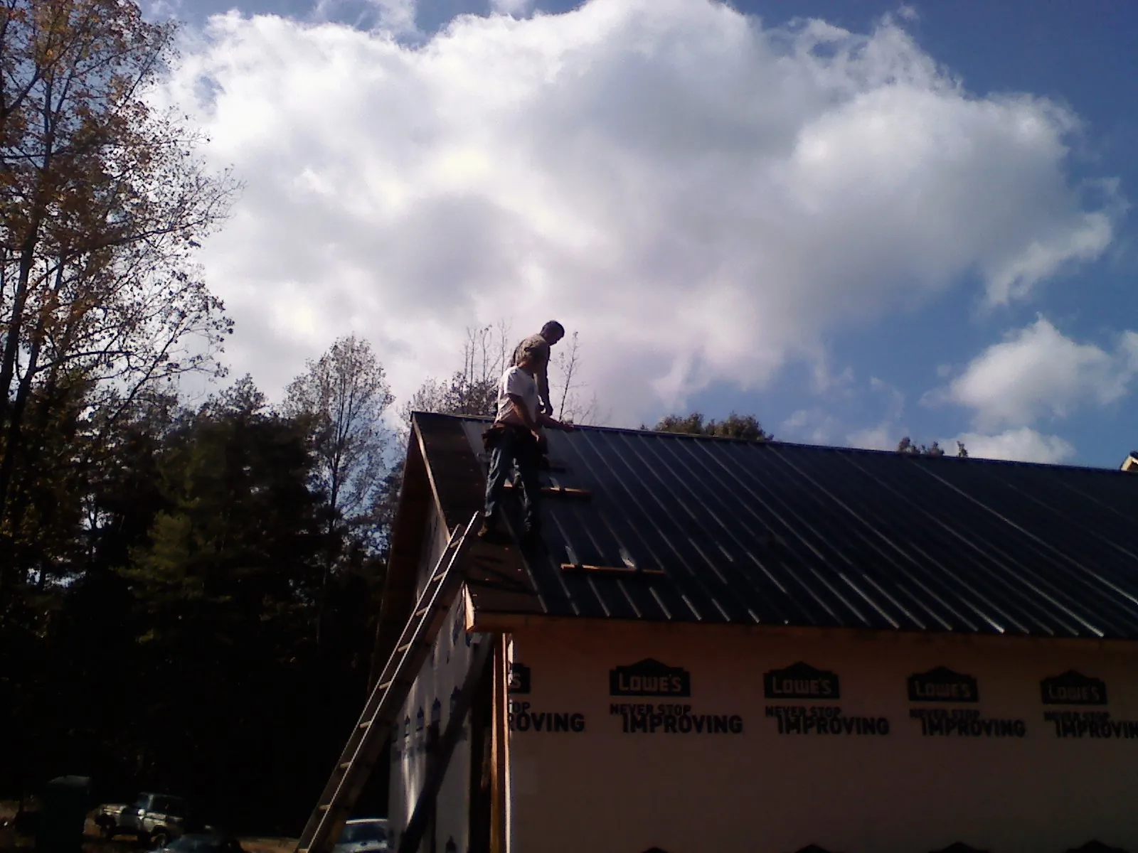 Roofer fastening dark metal panels high against a cloudy sky, from a Roof Inspection job in Willow City
