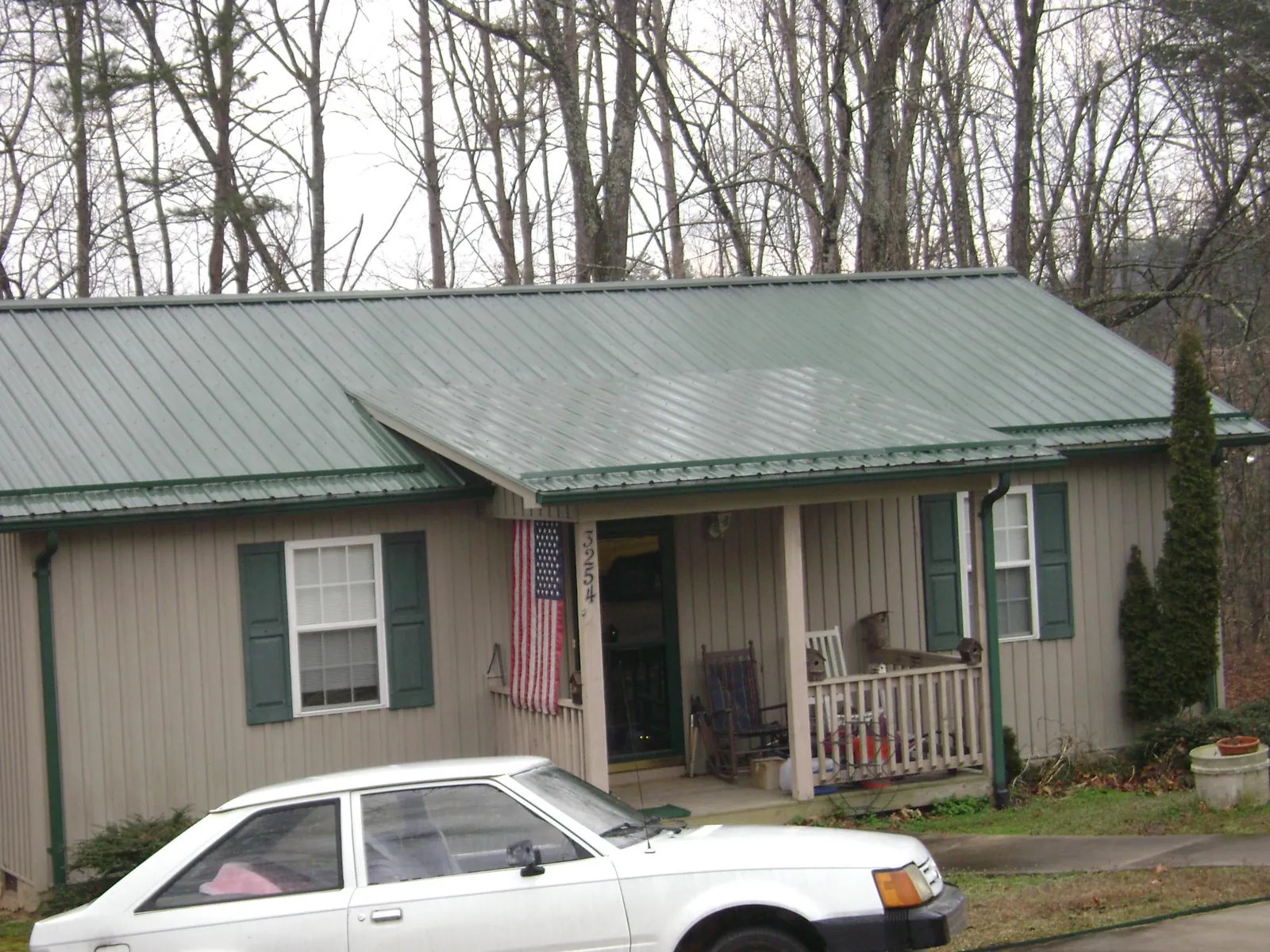 Green metal roof and front porch on a tan sided cottage in Willow City